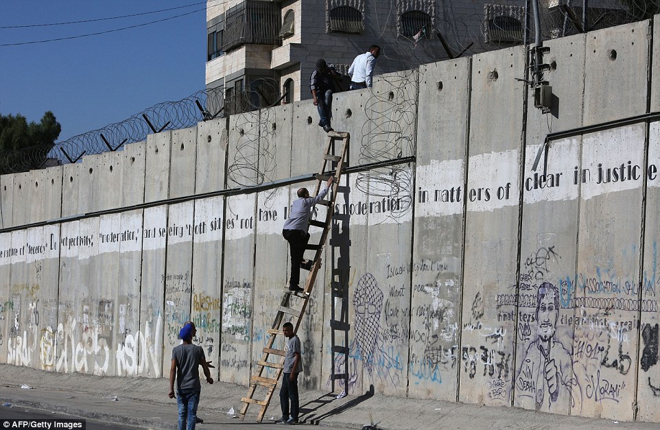 Symbol of aggression: Palestinians climb over a section of Israel